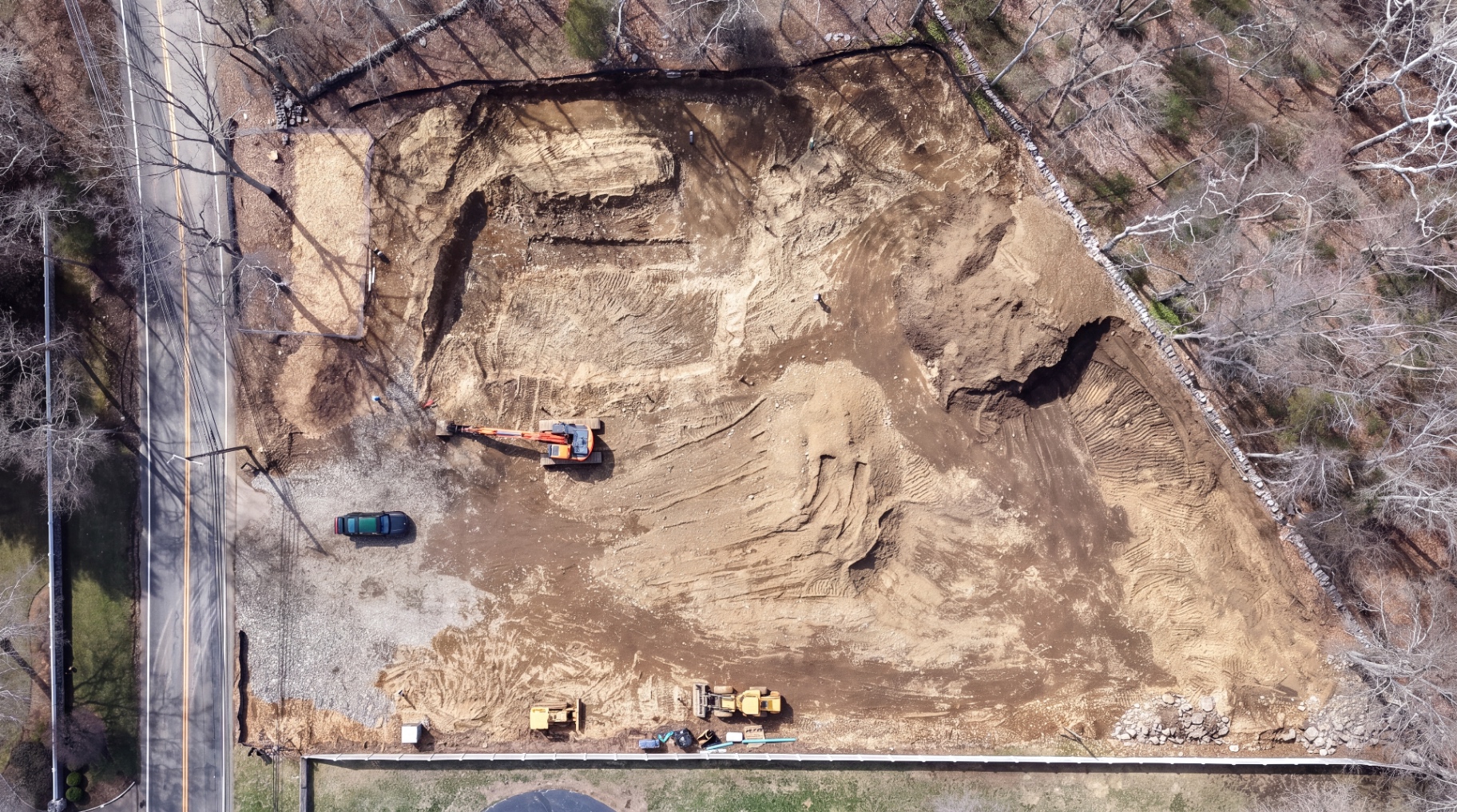 Aerial view of the cleared site with an excavator beginning bulk excavation.